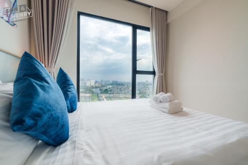 a bed with blue pillows and a large window at Son&Henry Zenity District 1 in Ho Chi Minh City