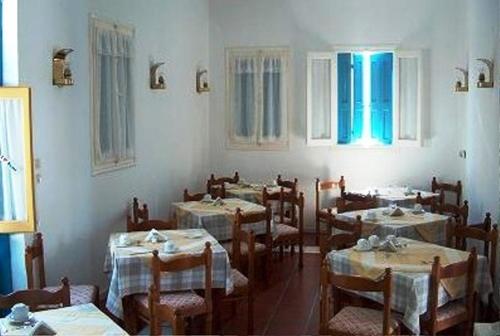 uma sala de jantar com mesas, cadeiras e janelas em Horio Village Rooms em Simi