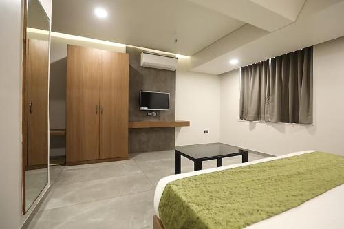 Hotel R City Inn By Mantram Hospitality في راجكوت: غرفة نوم بسرير وتلفزيون وطاولة