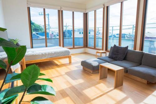 a living room with a couch and tables and windows at 葉山 森戸海岸すぐの富士山と海が一望できる新築ヴィラ bbq サウナ in Hayama
