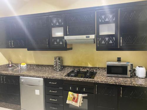 - une cuisine avec des placards noirs, une cuisinière et un four micro-ondes dans l'établissement Appartement Ensoleillé vue Piscine, à Marrakech