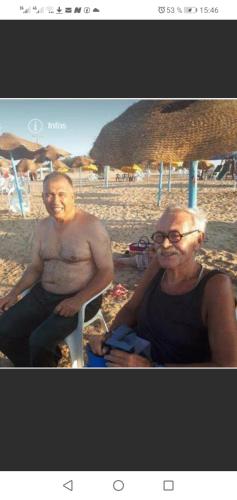 zwei Männer sitzen am Strand vor einem Sonnenschirm in der Unterkunft Venus house15 in Raoued