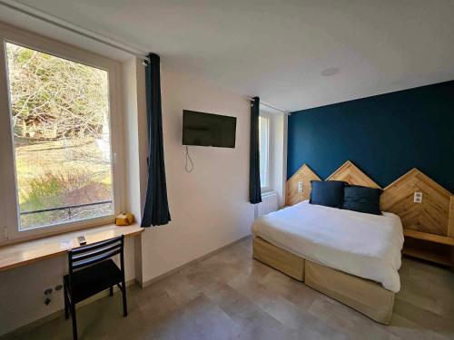 a bedroom with a bed and a desk and a window at Hôtel La bonne hôtesse in Chambon-sur-Lac