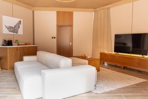 a living room with a white couch and a television at Pura Eco Retreat, Jebel Hafit Desert Park in Al Ain