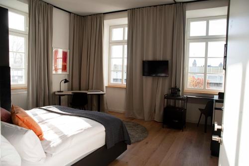 a bedroom with a bed and a desk and windows at YokoLou - Design-Apartments in Koblenz