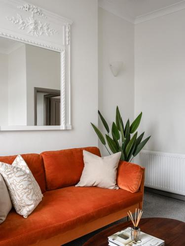 een oranje bank in een woonkamer met een spiegel bij Urban Rest Notting Hill Apartments in Londen