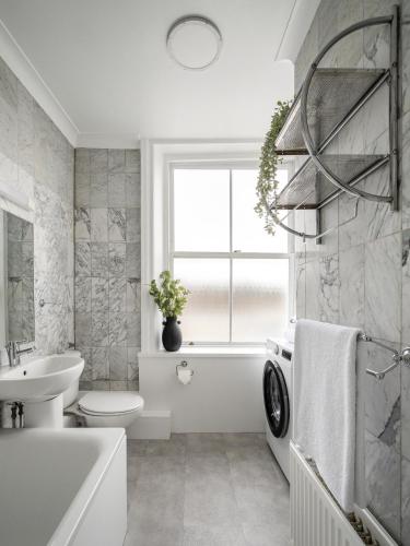 een badkamer met een wit bad, een wastafel en een wasmachine bij Urban Rest Notting Hill Apartments in Londen