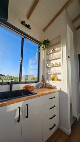 uma cozinha com armários brancos, uma janela e um lavatório em Coastal Haven - Port Fairy Tiny Homes em Killarney