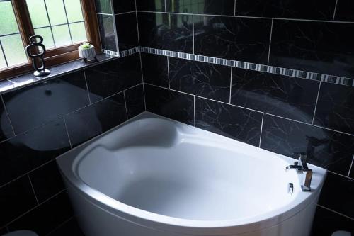 y baño de azulejos negros con bañera blanca. en Home in Rugby Warwickshire, 