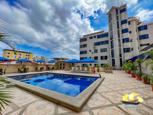 a pool in front of a building with blue umbrellas at Hotel Bucaneiro in Manta