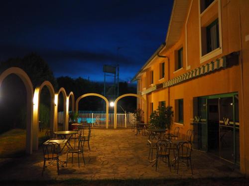 a patio with chairs and tables and a building at night at N'Atura Hôtel in Aire-sur-lʼAdour