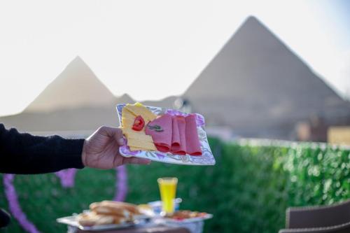 a hand holding a piece of cake and a plate of food at pyramids light show in Cairo