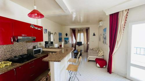 eine Küche mit roten Schränken und ein Wohnzimmer in der Unterkunft Bungalow S+1 au port de Kantaoui, Sousse. Avec balcon offrant une panorama envoûtant in Sousse