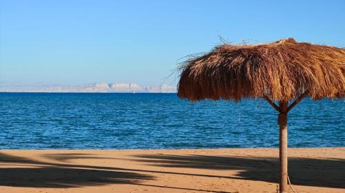 a straw umbrella on a beach near the water at Luxury Chalet in Mountain View 2 , El-Sokhna with Sea View , Pool View and Garden View Families Only in Ain Sokhna