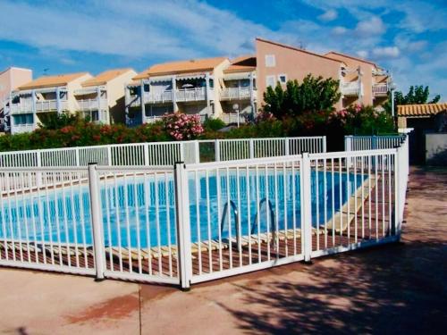 une clôture blanche avec une piscine en face de certains condos dans l'établissement Le Scarlett - Piscine, parking et proche plage, à Palavas-les-Flots