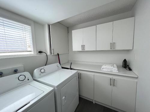 uma cozinha com armários brancos e uma máquina de lavar e secar roupa em Cozy Suite Near Airport Calgary em Calgary