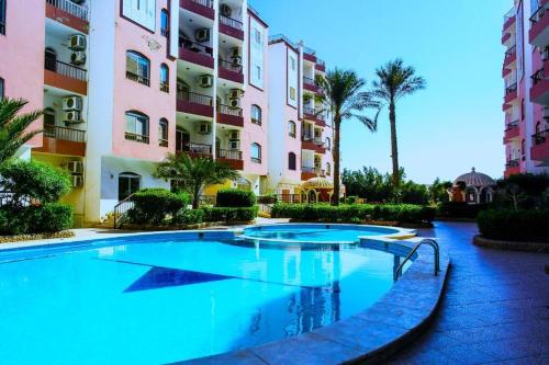 a swimming pool in front of a building with palm trees at Desert Pearl Romantic Apartment in Hurghada