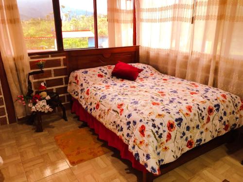 a bedroom with a bed with a floral comforter and a window at Hospedaje Valentina para ti y tu familia in Mera