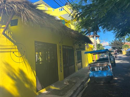 a yellow building with a car parked in front of it at Coco Hotel and Hostel in Sosúa