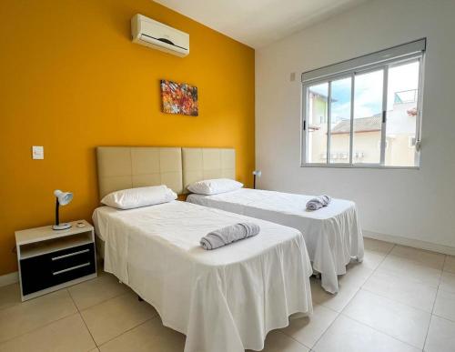 two beds in a room with yellow walls and a window at Aguas do Santinho Residence - Praia do Santinho in Florianópolis
