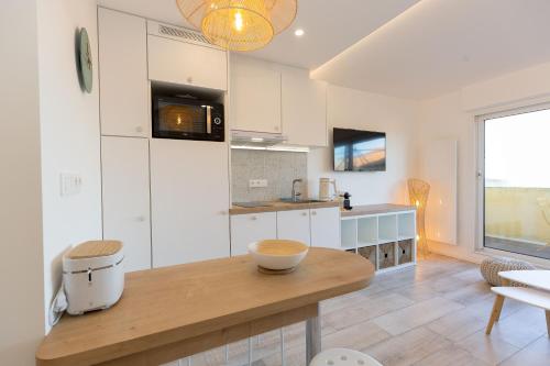 une cuisine avec des armoires blanches et une table en bois dans l'établissement Atlantic Selection - La Parenthèse de Capbreton - Vue océan, plage Notre-Dame, à Capbreton
