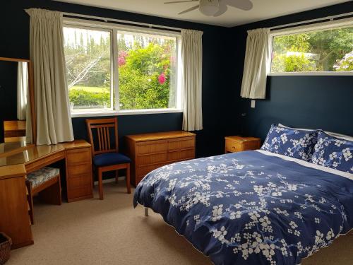 a bedroom with a bed and a desk and windows at TayFord Cottage in Waipu