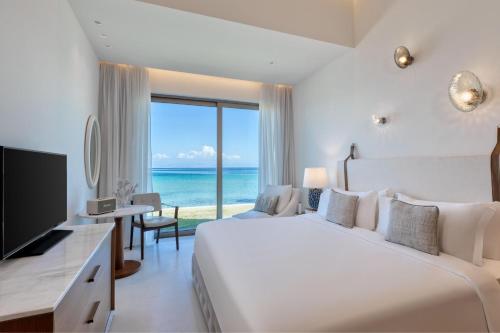 a bedroom with a bed and a television and the ocean at Domes Miramare, a Luxury Collection Resort, Corfu - Adults Only in Moraitika