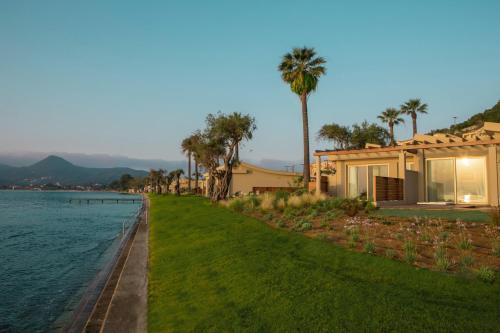 a house next to a body of water with palm trees at Domes Miramare, a Luxury Collection Resort, Corfu - Adults Only in Moraitika