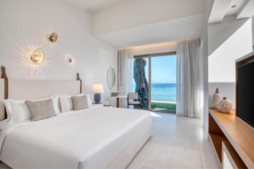 a white bedroom with a large bed and a view of the ocean at Domes Miramare, a Luxury Collection Resort, Corfu - Adults Only in Moraitika