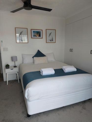 a bedroom with a large white bed with a ceiling fan at Sandy Shores Holiday Units in Caloundra