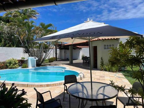 een patio met een tafel en een parasol naast een zwembad bij Casa di Barra in Barra de São Miguel