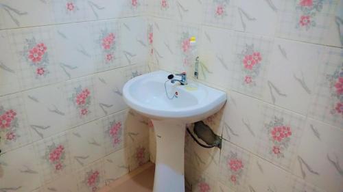 lavabo blanco en el baño con flores rosas en la pared en Studio privatif spacieux en air de plage, en Cotonou