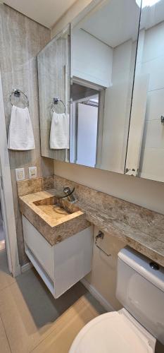 a bathroom with a sink and a toilet and a mirror at Apartamento Finamente Mobiliado - perto da praia in Balneário Camboriú