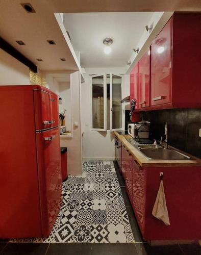 Il comprend une cuisine dotée de placards rouges et de carrelage noir et blanc. dans l'établissement Appartement au coeur de Ménilmontant, à Paris