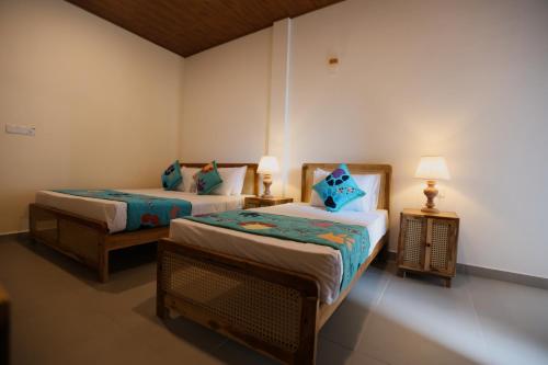 two beds in a room with two lamps on tables at Coop Safari Hotel in Tissamaharama