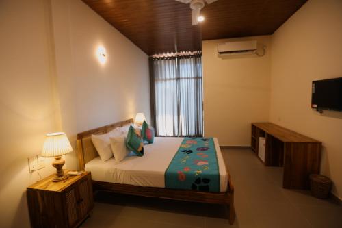 a bedroom with a bed with a lamp and a television at Coop Safari Hotel in Tissamaharama