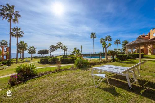 eine weiße Bank in einem Park mit Palmen in der Unterkunft Apartment Los Molinos on the beachfront with pool in Estepona