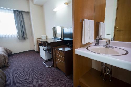 a bathroom with a sink and a desk with a bed at Minami Fukuoka Green Hotel in Fukuoka