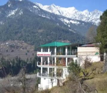 a building on a hill with mountains in the background at Hotel Manali Jain Cottage in Manāli