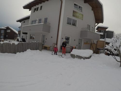 a woman and two children standing in the snow in front of a house at Ferienhaus Bergauf with Hot Tub in Neukirchen am Großvenediger