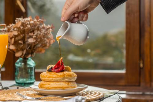 a person pouring syrup onto a stack of pastries at Angelats Hotel - A Signature Boutique Hotel & Restaurant in Ribes de Freser