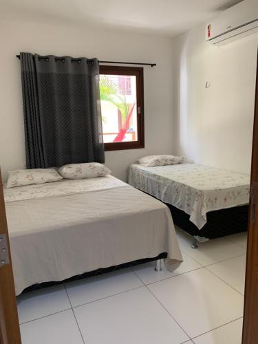 two beds in a white room with a window at Flat Barra do Cunhaú in Canguaretama