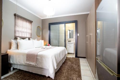 a bedroom with a large white bed and a bathroom at URlyfstyle Cottage Near OR Tambo International Airport in Kempton Park