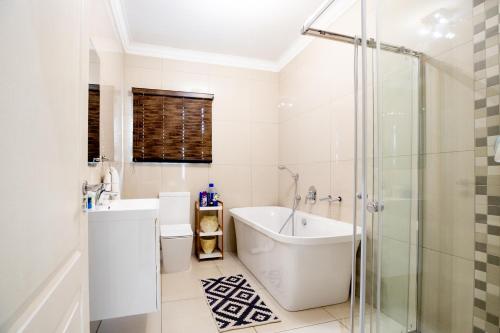 uma casa de banho branca com uma banheira e um chuveiro em URlyfstyle 5 bedrooms near OR Tambo international Airport em Kempton Park