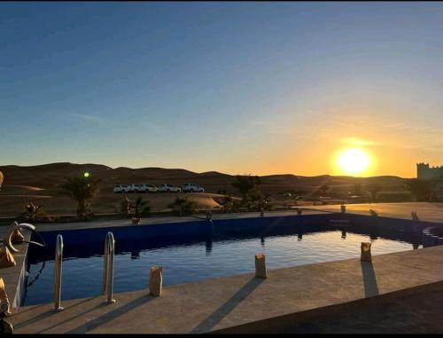einen Pool mit Sonnenuntergang im Hintergrund in der Unterkunft كعب غزال in Merzouga