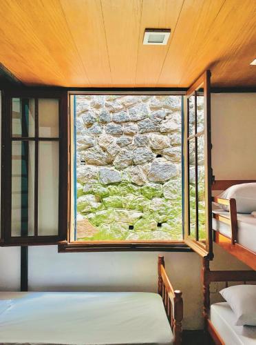 a room with two beds and a window with a stone wall at Hostel Sunrise in Rio de Janeiro