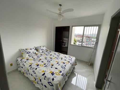 a bedroom with a bed with a comforter and a window at Quarto e sala 100 mts da praia in Guarapari