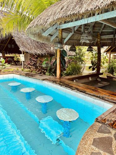 a swimming pool in a resort with a thatched roof at Eco Glamping Treehouses Closest Resort To All Tourist Attractions in Balilihan