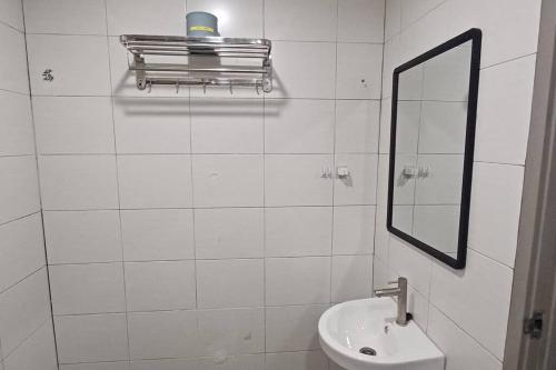 La salle de bains est pourvue de carrelage blanc, d'un lavabo et d'un miroir. dans l'établissement Grand Suite @ The CEO Penang, à Bayan Lepas