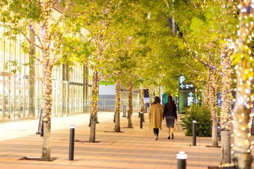 two people walking down a sidewalk with trees and lights at Villa Fontaine Grand Tokyo Ariake in Tokyo